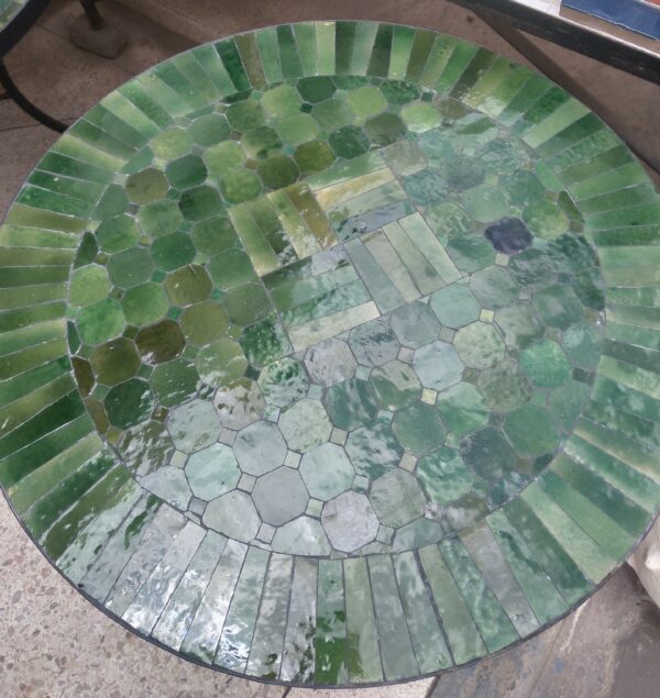 Photo d'une table en fer forgé avec un plateau en zellige, c'est un assemblage de pièces de faïence, mosaïque entièrement taillé et incrusté sur un support en mortier.