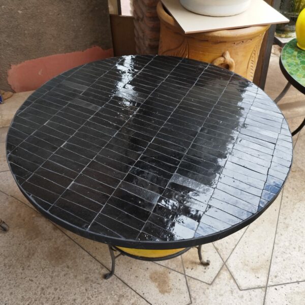 Photo d'une table en fer forgé avec un plateau en zellige, c'est un assemblage de pièces de faïence, mosaïque entièrement taillé et incrusté sur un support en mortier.