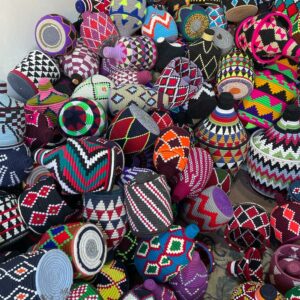 Photo de boîtes berbère, arrondie, avec un chapeau, souple réalisé avec la plante du doum, un palmier nain, avec lequel la vannerie est fabriqué au Maroc. Ensuite une broderie en laine de couleurs vive aux rosaces multiple, viennent êtres brodées, tellement original, par sa forme, comme par ses motifs géométriques. Objet de décoration intérieur, vide poche.