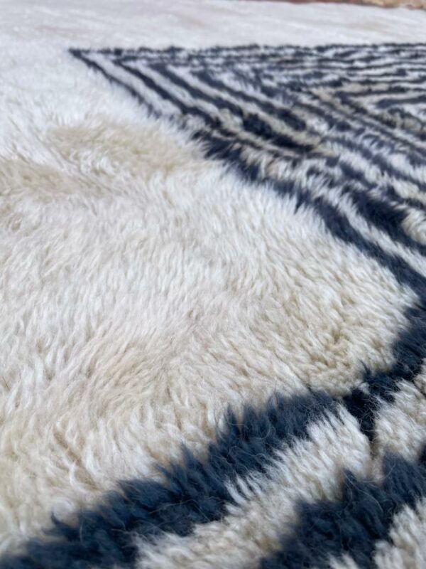 Photo d'un tapis Mrirt rayé camaïeu de bleu et gris, ligne géométrique, sur fond écru. Les tapis Mrirt sont tissé avec des nœuds doubles ce qui en fait des tapis particulièrement dense.