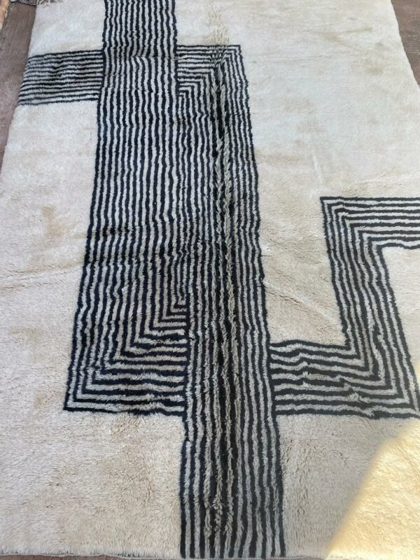 Photo d'un tapis Mrirt rayé camaïeu de bleu et gris, ligne géométrique, sur fond écru. Les tapis Mrirt sont tissé avec des nœuds doubles ce qui en fait des tapis particulièrement dense.