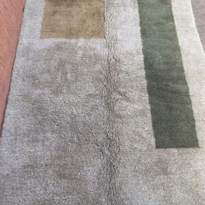 Photo d'un tapis Mrirt taupe et kaki grand motif carré et grand rectangle sur le côté. Le tapis Mrirt est un tapis à poil long ( shaggy ) tissé avec des doubles nœuds, entièrement réalisé à la main, dans l'atlas au Maroc. 280X185. 1390 €