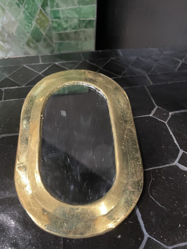 Photographie d'un miroir à sac avec un contour cuivre, en forme ovale.