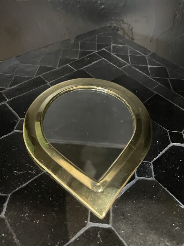 Photographie d'un miroir à sac avec un contour cuivre, en forme de goutte.