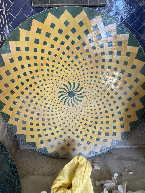 Photographie d'un plateau de table en zellige jaune et bleu, les motifs forme une rosace.
