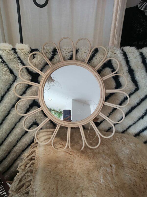 Photographie d'un miroir rond en osier en forme de fleur. les pétales sont arrondies.