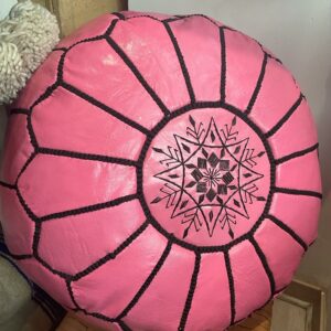 Photo d'un pouf en cuir rose marocain, il est brodé de large bande noir, au centre un rond brodé entoure une rosasse brodé. Sa couleur lui donne plus de modernité, et du pep's dans un intérieur.