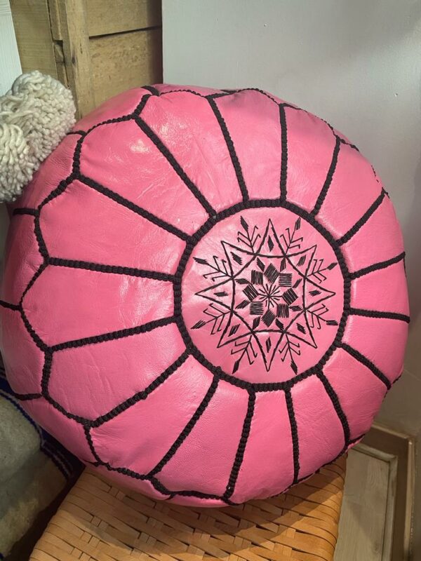 Photo d'un pouf en cuir rose marocain, il est brodé de large bande noir, au centre un rond brodé entoure une rosasse brodé. Sa couleur lui donne plus de modernité, et du pep's dans un intérieur.