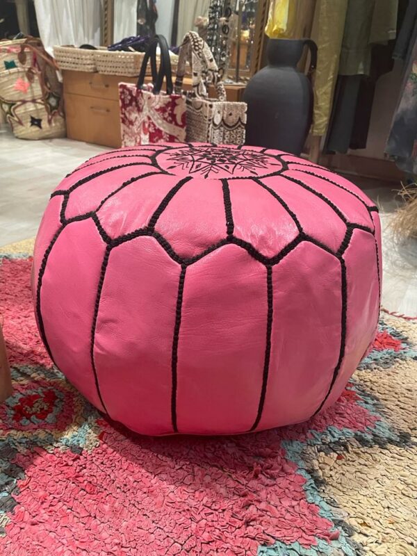 Photo d'un pouf en cuir rose marocain, il est brodé de large bande noir, au centre un rond brodé entoure une rosasse brodé. Sa couleur lui donne plus de modernité, et du pep's dans un intérieur.