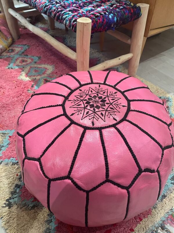 Photo d'un pouf en cuir rose marocain, il est brodé de large bande noir, au centre un rond brodé entoure une rosasse brodé. Sa couleur lui donne plus de modernité, et du pep's dans un intérieur.