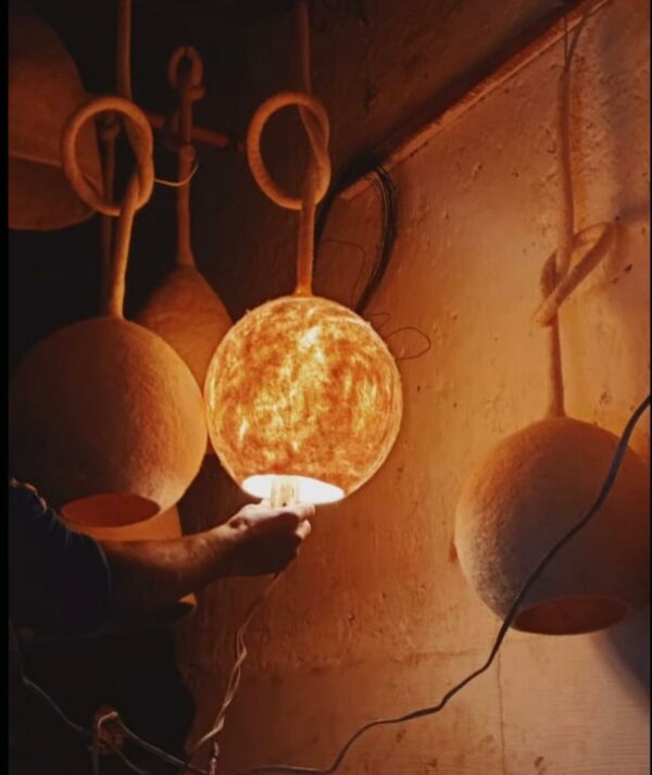 Photographie d'une suspension en feutre de laine en forme de boule écru. La laine est modelée à la main jusqu'à ce qu'elle devienne ce qu'on appelle de la laine feutrée. Avec ce luminaire, vous pouvez créer une ambiance naturelle et chaleureuse dans votre intérieur.