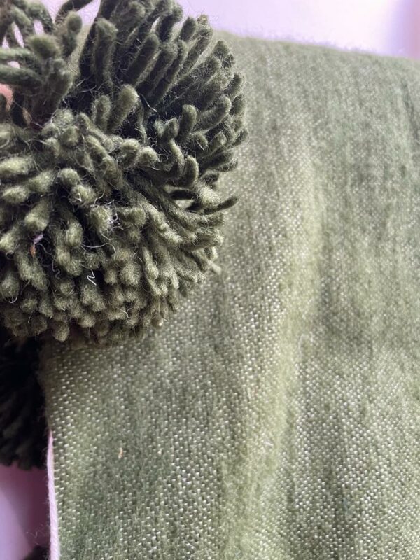 Photo d'un plaid en laine kaki, avec pompons.