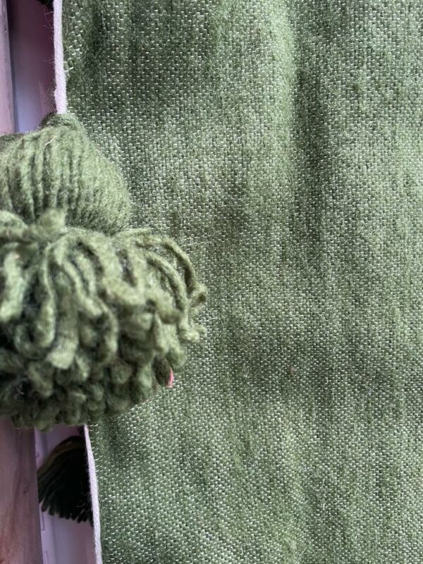 Photo d'un plaid en laine kaki, avec pompons.