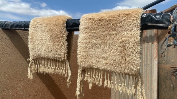 Tapis Mrirt beige éclat soleil disposé sur des rondins de bois pour un sechage au soleil